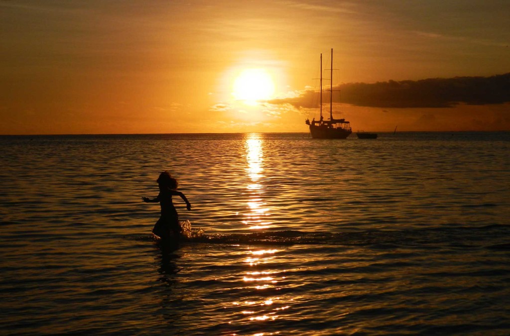 Menina corre no mar enquanto sol se põe na praia principal da Ilha de Mana
