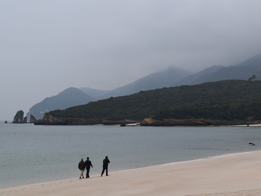 Pessoas agasalhadas caminham pela areia em dia nublado